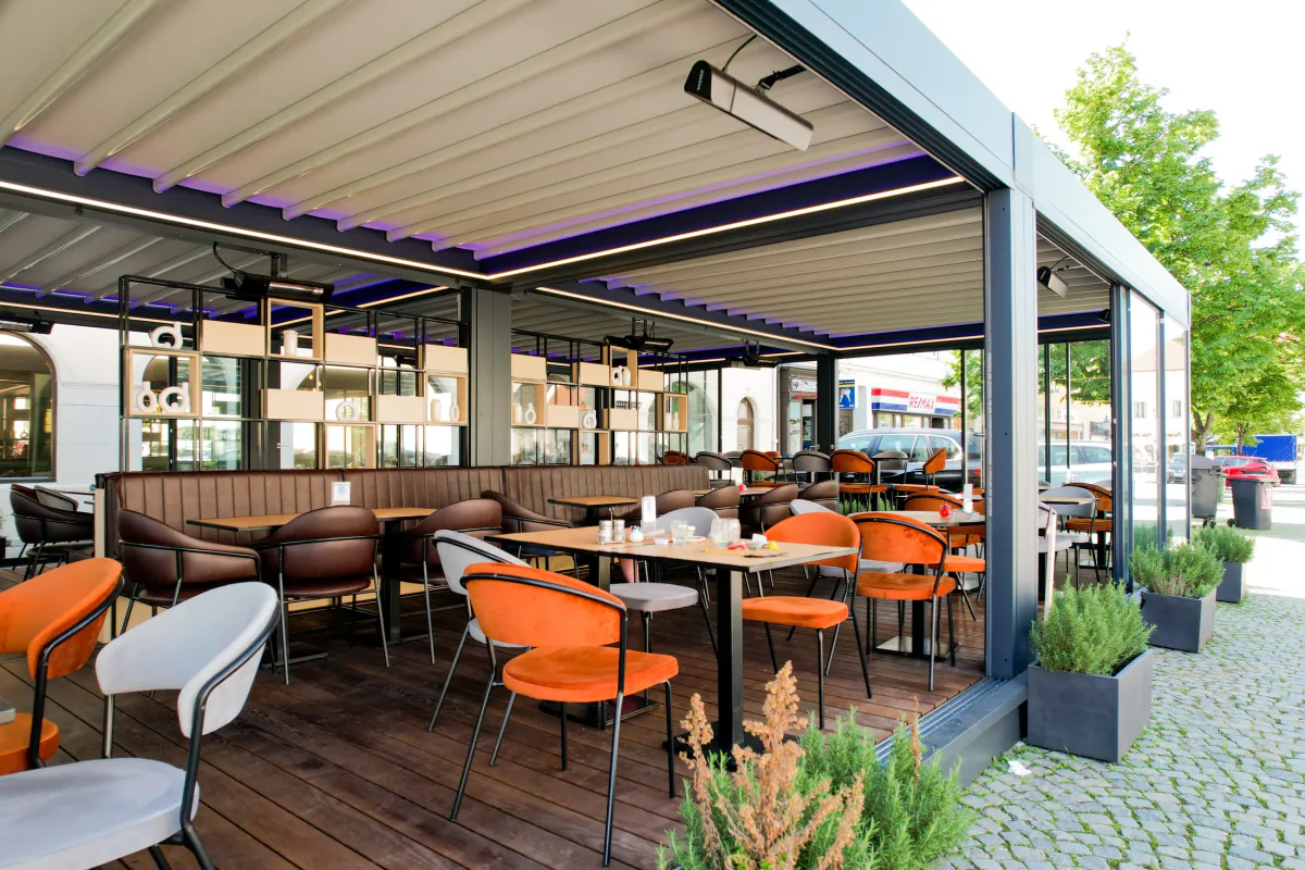 Pizzeria Haas, Bruck an der Leitha – Eckansicht mit Lamellendach, Glaselementen und orangefarbenen Sitzplätzen